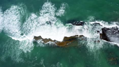 Beautiful-bird's-eye-top-aerial-drone-static-shot-of-waves-crushing-into-a-black-rock-in-the-beach-at-Sibauma-creating-a-natural-swimming-pool-during-low-tide-near-Pipa-in-Northern-Brazil