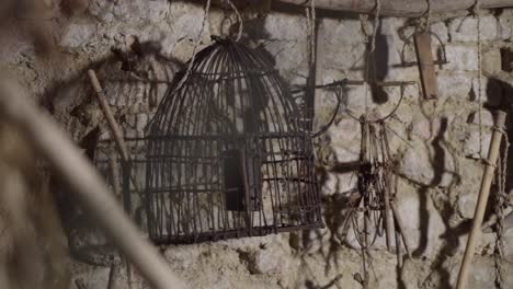Vintage-Birds-Cage-Against-Wall-Of-Stones-And-Other-Old-Tools