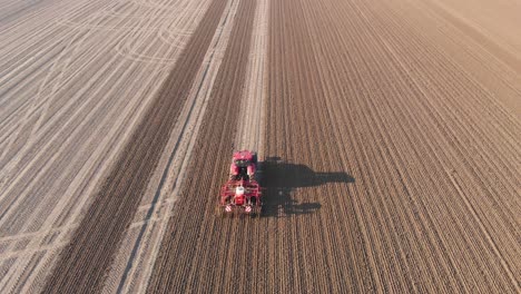 Drone-shot-of-red-tractor-plowing-brown,-earthy,-dutch-farmland