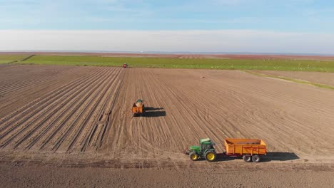 Drone-shot-of-tractors,-farmers-working-on-brown,-earthy-farmland,-plowing-and-harvesting
