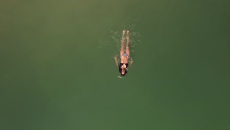 Luftaufnahme-Von-Oben-Nach-Unten-Tracking-Frau-Im-Bikini-Entspannendes-Schwimmen-In-Der-Wunderschönen-Grünen-Wasseroberfläche-Des-Ozeans