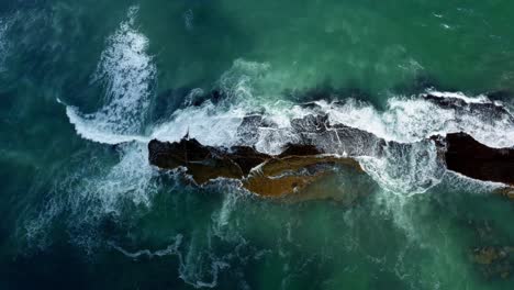 Beautiful-bird's-eye-top-aerial-drone-shot-of-waves-crushing-into-a-black-rock-in-the-beach-at-Sibauma-creating-a-natural-swimming-pool-during-low-tide-near-Pipa-in-Northern-Brazil