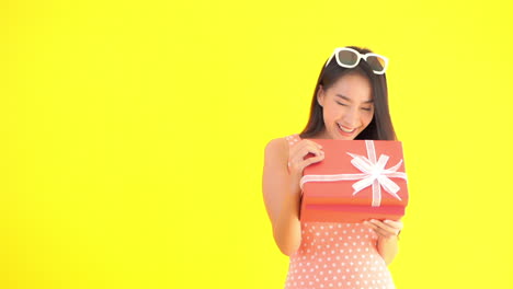 A-young-attractive-Asian-woman-in-a-sundress-and-sunglasses-opens-a-beautifully-wrapped-present-reacting-in-joy