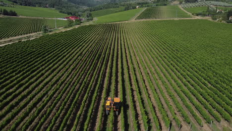 Yellow-Tractor-At-Work,-Trimming,-And-Cultivating-Narrow-Rows-Of-Green-Vineyards-In-Tuscany-Hills,-Italy