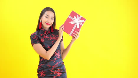 A-young-woman-in-a-silk-black-and-red-dress-holds-up-a-wrapped-present