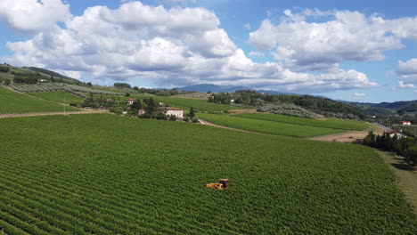 Yellow-Tractor-Working-On-The-Narrow-Rows-Of-Green-Vineyards-Under-The-Beautiful-Sky-In-Tuscany-Hills,-Chianti-Frescobaldi,-Italy