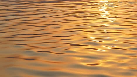 Beautiful-cinematic-close-up-shot-of-holy-river-Ganges-during-sunrise-time-making-the-water-shine-all-gold-with-the-ripples