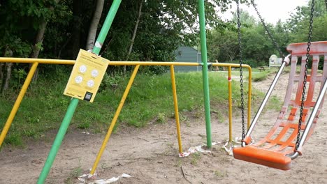 Public-warning-covid-corona-virus-sign-on-park-playground-with-empty-swing