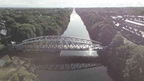 Aerial-descending-view-towards-scenic-old-vintage-steel-archway-traffic-footbridge-over-Manchester-ship-canal-crossing