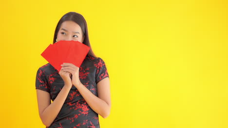 Asiatische-Frau,-Die-Eine-Traditionelle-Chinesische-Kleidung-Trägt,-Die-Das-Chinesische-Neujahr-Feiert-Und-Ihr-Gesicht-Mit-Roten-Papieren-Oder-Gutscheinen-Bedeckt