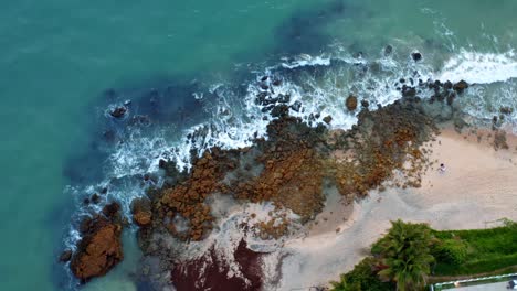 Beautiful-passing-bird's-eye-view-of-ocean-waves-hitting-rocks-on-the-shore-of-a-tropical-Northern-Brazil-beach-named-Tabatinga-with-blue-water-and-golden-sand-near-Joao-Pessoa-on-a-warm-summer-day