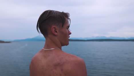 Slow-motion-shot-of-a-young-man-with-water-dripping-off-of-his-face,-wearing-a-silver-necklace,-staring-into-beautiful-seascape,-taking-in-the-moment-and-embracing-the-feeling-of-life-and-freedom