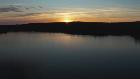 Drone-flying-over-a-quiet-lake-going-towards-a-colorful-sunset,-in-the-Eastern-Township,-Quebec,-Canada
