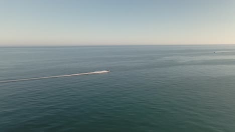 Fast-aerial-view-following-speeding-jet-ski-across-seascape-ocean-horizon