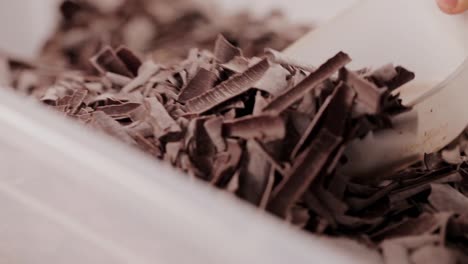 Baker-Chef-grabs-vegan-tasty-chocolate-pieces-with-plastic-scoop-inside-food-container-close-up-shoot