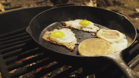 Two-Eggs-and-English-Muffin-being-cooked-in-frying-pan-over-on-campfire