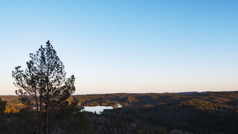 Shadows-cover-forest-and-lake-landscape-as-sun-goes-down,-Norway-time-lapse