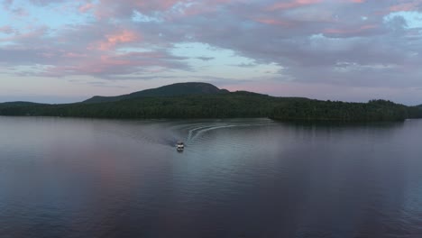 Aerial-shot-going-around-a-lonely-boat-on-a-beautiful-lake-with-a-colorful-sky-in-the-Eastern-Township,-Quebec,-Canada