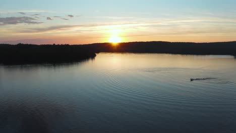 Drone-shot-over-a-beautiful-sunset-on-a-lake-with-a-single-boat-waterskier-in-Quebec,-Canada