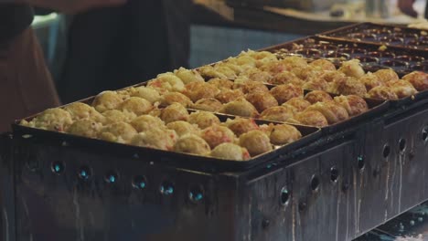 Hands-Of-Chef-Cooking-Japanese-Snack-Food,-Takoyaki-Being-Cooked-In-A-Fried-Pan-In-The-Food-Market-In-Kyoto,-Japan