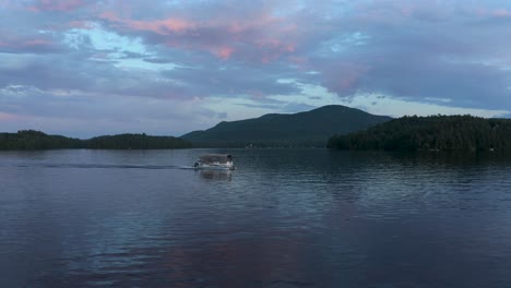Drone-flying-in-front-of-a-lonely-boat-at-dusk-on-a-lake-with-a-colorful-sky-in-the-Eastern-Township,-Quebec,-Canada