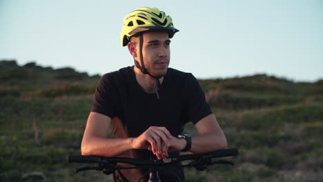 Male-biker-with-helmet-enjoy-rest-after-long-ride-at-dusk,-handheld