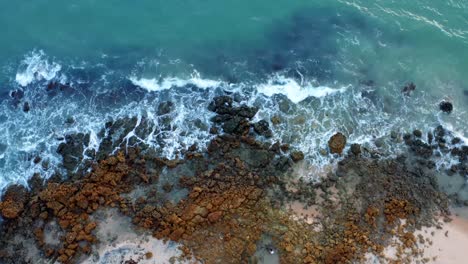 Beautiful-lowering-bird'd-eye-view-of-ocean-waves-hitting-rocks-on-the-shore-of-a-tropical-Northern-Brazil-beach-named-Tabatinga-with-blue-water-and-golden-sand-near-Joao-Pessoa-on-a-warm-summer-day