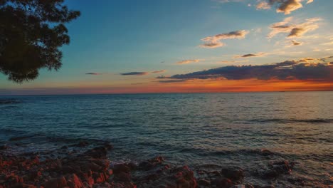 Time-lapse---hyper-lapse-of-the-sun-setting-over-the-horizon-at-a-romantic-beach-with-small-waves-at-the-Croatian-Mediterranean-seaside-with-pine-trees-and-ships-passing-by