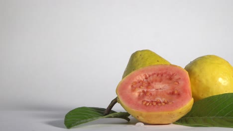 Fruta-De-Guayaba-Entera-Y-Media-Aislada-En-Fondo-Blanco,-Alejamiento-Lento