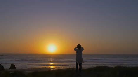Man-in-kaftan-stares-at-breathaking-sunset-over-ocean-horizon,-wide