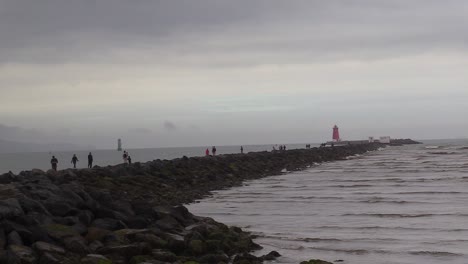 People-walking-along-the-coast-or-south-wall-to-a-lighthouse-on-Dublin's-coastline