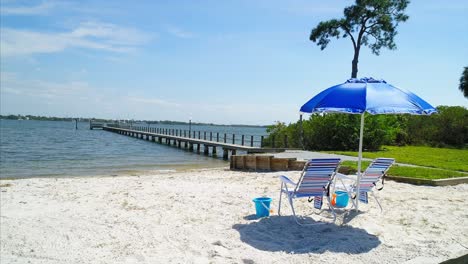 Beach-chairs-and-umbrella-on-a-beach-next-to-a-pier-by-a-water-vista