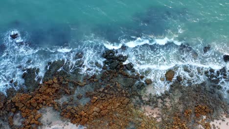 Beautiful-rising-bird's-eye-view-of-ocean-waves-hitting-rocks-on-the-shore-of-a-tropical-Northern-Brazil-beach-named-Tabatinga-with-blue-water-and-golden-sand-near-Joao-Pessoa-on-a-warm-summer-day