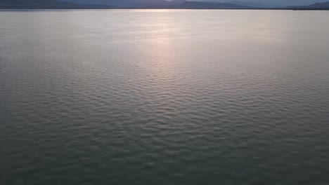 Scenic-Utah-lake-water-rippling-on-surface-with-mountain-range-in-background-at-sunset,-overhead-aerial-tilt-up