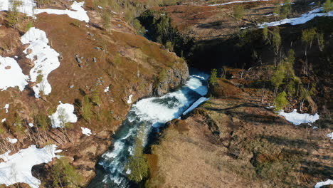 Aerial-view-overlooking-a-waterfall-in-snowy-nature,-sunny,-summer-day,-in-the-Lyngen-alps,-North-Norway---Pull-back,-drone-shot