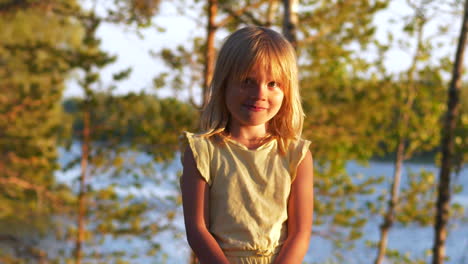 A-shy-blonde-little-girl-is-facing-the-camera-at-sunset,-golden-nordic-hour