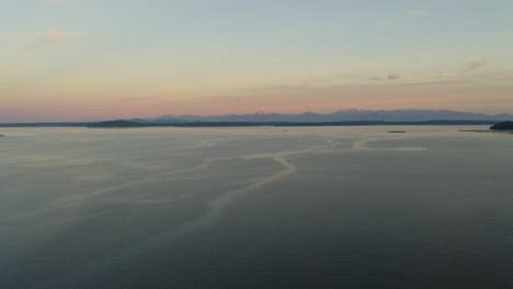 Gradual-Pan-Right-Reveals-Silhouette-of-Pacific-Coast-Mountain-Range-in-Distance-as-Drone-Flies-Above-Puget-Sound-in-Washington-State,-Aerial