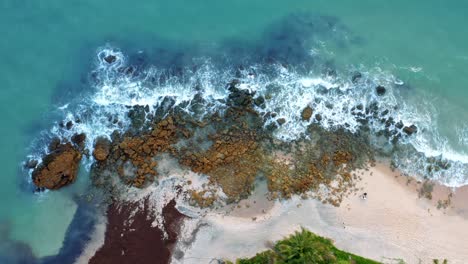 Beautiful-top-bird's-eye-view-of-ocean-waves-hitting-rocks-on-the-shore-of-a-tropical-Northern-Brazil-beach-named-Tabatinga-with-blue-water-and-golden-sand-near-Joao-Pessoa-on-a-warm-summer-day