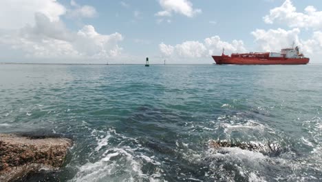 An-industrial-ship-floats-into-the-channel-between-jetties-as-waves-lap-up-onto-the-granite-rocks-in-Port-Aransas,-Texas-on-the-Gulf-of-Mexico