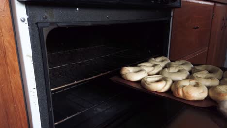 Hands-with-oven-mitts-remove-a-tray-of-fresh-baked-bagels-from-home-oven