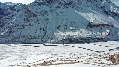 Aerial-shot-of-a-man-walking-on-a-helipad-covered-with-snow-revealing-huge-mountains-of-spiti-in-the-background
