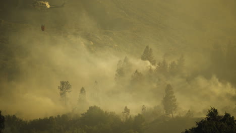 Wind-blowing-thick-wildfire-smoke-across-dry-valley-with-helicopter-firefighting