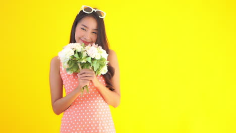 A-cute-young-woman-in-a-sundress-holds-a-bouquet-of-flowers-raising-them-to-smell