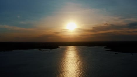 Stunning-aerial-drone-static-shot-of-a-golden-sunset-reflecting-onto-the-water-of-a-large-amazonian-river-in-Joao-Pessoa,-Brazil