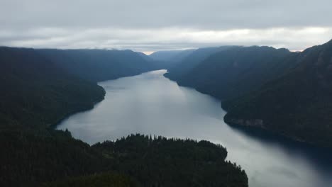 Drone-Vuela-Más-Allá-De-La-Cornisa-De-La-Montaña-Sobre-Un-Gran-Lago-Azul-En-Un-Día-Nublado,-Lago-Crescent,-Parque-Nacional-Olímpico,-Washington