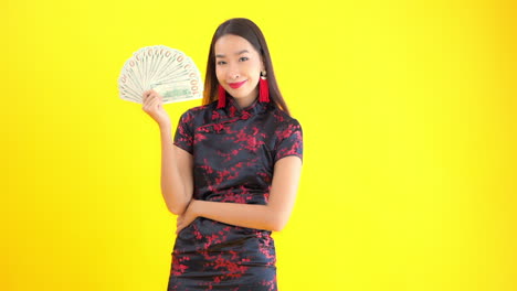 Holding-a-fan-full-of-one-hundred-dollar-bills,-an-attractive-young-woman-keeps-her-self-cool