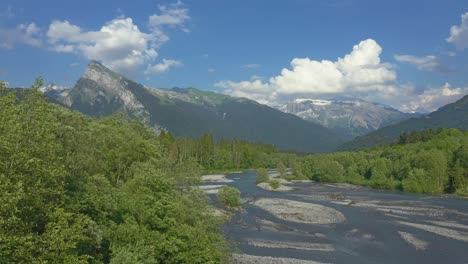 Luftbild-über-Dem-Giffre-Fluss-In-Den-Französischen-Alpen,-Der-über-Den-Wunderschönen,-Leuchtend-Grünen-Frühlingsbäumen-Mit-Einem-Wunderschönen-Blick-Auf-Die-Berge-Des-Criou-Im-Hintergrund-Fliegt