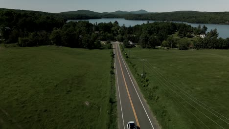A-White-Car-Driving-On-The-Asphalt-Road-In-Quebec,-Canada-On-A-Bright-Weather---ascending-drone-shot