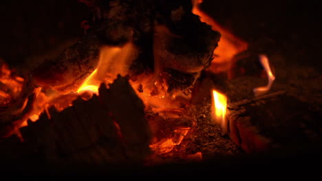 Nachtaufnahme-Von-Glühenden-Lagerfeuerflammen,-Die-Aus-Glühenden-Roten-Kohlen-Brennen,-Wobei-Ein-Paar-Kleine-Funken-Aus-Dem-Feuer-Fliegen