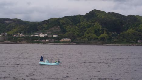 Kleines-Fischerboot,-Das-Auf-Dem-Ruhigen-Wasser-Am-Meer-Schwimmt,-Mit-Grünen-Berghügeln-Im-Hintergrund